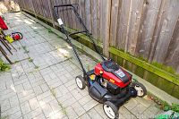 Full side view of the Craftsman push lawn mower on outdoor stone tile ground near a wooden fence.