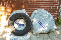 Four tires leaning against brick wall, one unwrapped and three wrapped in plastic covers