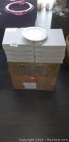 Stack of eight white boxed 8-inch round LED panel lights on top of a large cardboard box.