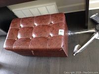 Overall view of brown leather ottoman with tufted top and studs along edge, showing size and condition.
