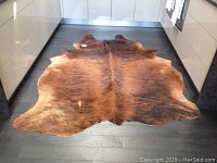 Full view of brown and tan cowhide rug laid on dark hardwood floor