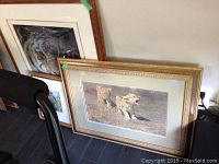 Three framed animal prints leaning against a wall, two show lions and one shows a wolf's face. Frames appear worn.