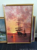 Full view of the large oil painting with two sailing ships and a small rowboat at sunset, set in a gold frame.
