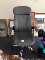 Front view of black leather office chair with padded headrest and armrests. Number tag visible on seat.