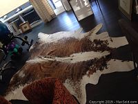 Full view of cowhide rug laid on dark floor next to furniture