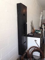 Side view of the tall narrow black storage unit mounted on the wall, showing its slim profile and height.