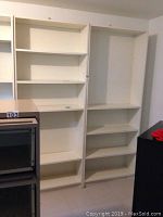 Two white wooden shelving units with multiple adjustable shelves, showing wear and scratches on the finish.