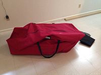 Large red fabric carrying bag lying on floor with zipper open slightly revealing artificial tree inside.