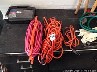 Photo of three extension cords coiled on a black surface, includes pink and orange cords with plugs and inline switches
