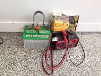 Items arranged on floor; shows Interstate Megatron battery, MotoMaster battery charger with cables and clips, and circuit breaker finder boxed.