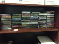 Shelf filled with stacked CD jewel cases of assorted music artists.