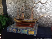 Photo of the fully assembled model ship displayed on top of the original box showing the hull's black and yellow paint and masts standing tall.