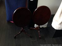 Two round mahogany end tables with fold-down tops and tripod bases seen from behind, showing their structure and color.