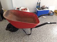 Red metal wheelbarrow showing full side profile on a garage floor.