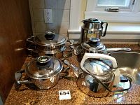 Photo of three Zepter Thermo-Control stainless steel pots with lids showing temperature gauges on lid handles, Russel Hobbs electric kettle, Alfi thermos on kitchen counter near sink.