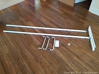 Photo shows two long straight poles, mounting hardware, and smaller extension pieces laid out on wooden floor.