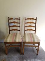 Two matching solid wood Ercol chairs side by side with striped cushions, natural wood finish, and ladder back design.