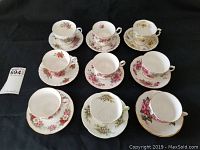 Photo of all nine tea cups and saucers arranged in rows on black background, showing floral patterns and size variations.