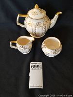 Full tea set showing teapot with lid, creamer, and sugar dish on black background with measurement tag