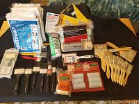 Full lot arranged neatly on black cloth background showing all paint brushes, roller covers, drop cloths, and sanding sheets in original packaging.