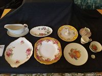 Full view of assorted china laid out on black cloth background including gravy boat, serving dishes, plates, and miniature teacups