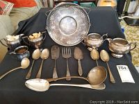 Full lot of assorted silver plated items arranged on table including spoons, ladles, creamer, sugar caddies, pie lifters and a handled tray.