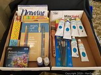 Box with art supplies including oil pastels, watercolor crayons, brushes, acrylic paints, and sketch pad.