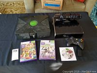 View of original Xbox with Xbox 360 console, Kinect sensor, controller, and three game titles visible on a table.