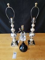 Two tall cracked look mirrored lamps and one smaller crystal diamond body lamp displayed on table against black background.