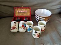 Full lot showing five geisha sake glasses, four dragon bowls, and two decorative massage balls in a box