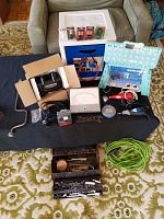 Multiple tools and equipment including socket wrench set, step stool, drill bit case, handheld tools, measuring tape, green extension cord and assorted accessories arranged on a dark cloth over patterned rug.