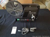 Full view of Chinon Sound 7500 film projector with reel mounted and power cord laid in front on black surface.