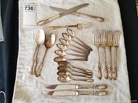 Full set of 20 silver plated cutlery pieces laid out on fabric, showing spoons, forks, and knives with floral ornate handles.
