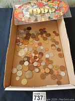 Box containing assorted loose coins of various sizes, colors, and types scattered inside.
