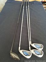 Four golf clubs on black cloth: three irons and one driver showing full length and heads