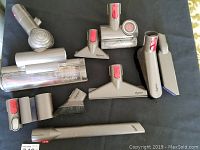Photo showing all nine Dyson vacuum attachments arranged on a dark surface with visible brand name and red locking buttons.