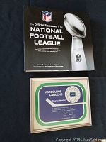 Photo of NFL Official Treasures book with black cover and white lettering along with the framed Vancouver Canucks Charter Member plaque.
