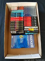 Box containing assorted new, sealed cassette tapes from brands Maxell, Fuji, Sony, JVC, TDK. All 60-minute tapes, unopened packaging.