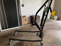 Overall side view of black hydraulic patient lift with caster wheels and base extended for stability to assist in lifting patients.