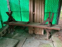 Photo of an extra long redwood picnic bench with cross-braced leg supports against a green backdrop.