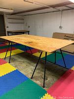 Full view of the plywood tabletop supported by two saw horses on a colorful foam mat floor.