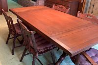 Photo showing the wooden dining table extended with one leaf and five chairs arranged around it with cushions on seats.