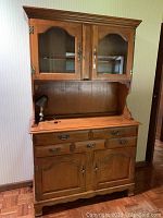 Front view of the wooden breakfront china cabinet showing glass upper doors, three drawers, and double lower wooden doors.