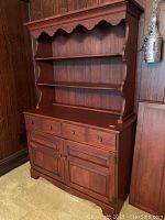 Wooden breakfront dining cabinet with open shelves, three drawers, and bottom cabinets against a wood-paneled wall.