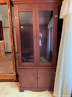 Front view of tall wooden china cabinet showing glass doors with shelves inside and wooden doors below.