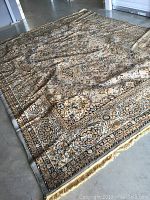 Photo of full rug laid out on smooth floor showing overall pattern and colors. Some fold creases visible.