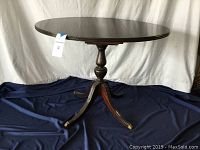 Full view of oval table top with drop leaf open on dark fabric background.