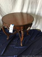 Full view of round wood end table showing ornate carved legs and apron with floral detail on tabletop.