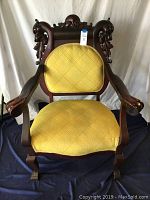 Front view of the detailed carved wooden armchair with yellow upholstery, showing dragon head armrest details.