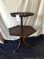Full side and angled view of the vintage two tiered hexagon accent table showing the twisted central column, hexagonal shelves with decorative gallery edges, and tripod base with brass-accented feet.